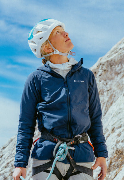 Woman in hemet and Montane jacket looking up at rock face
